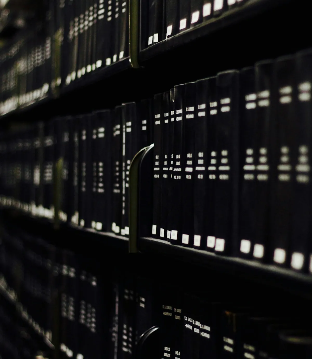 Black bound volumes on a shelf in low light