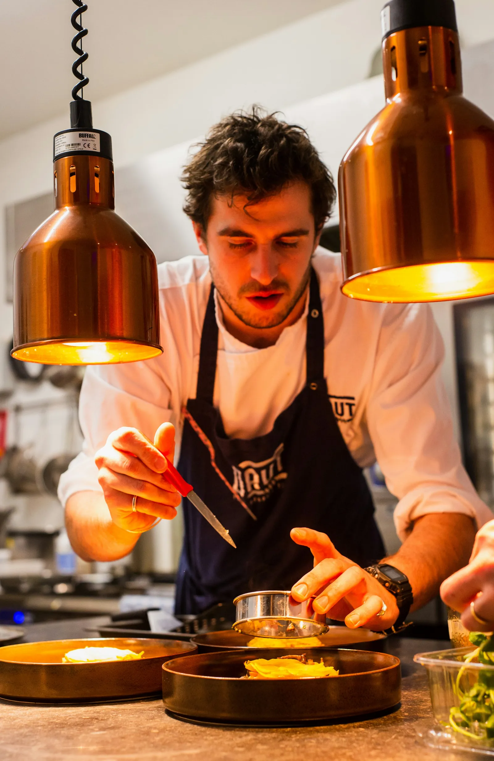 A chef plating dishes under copper lamps