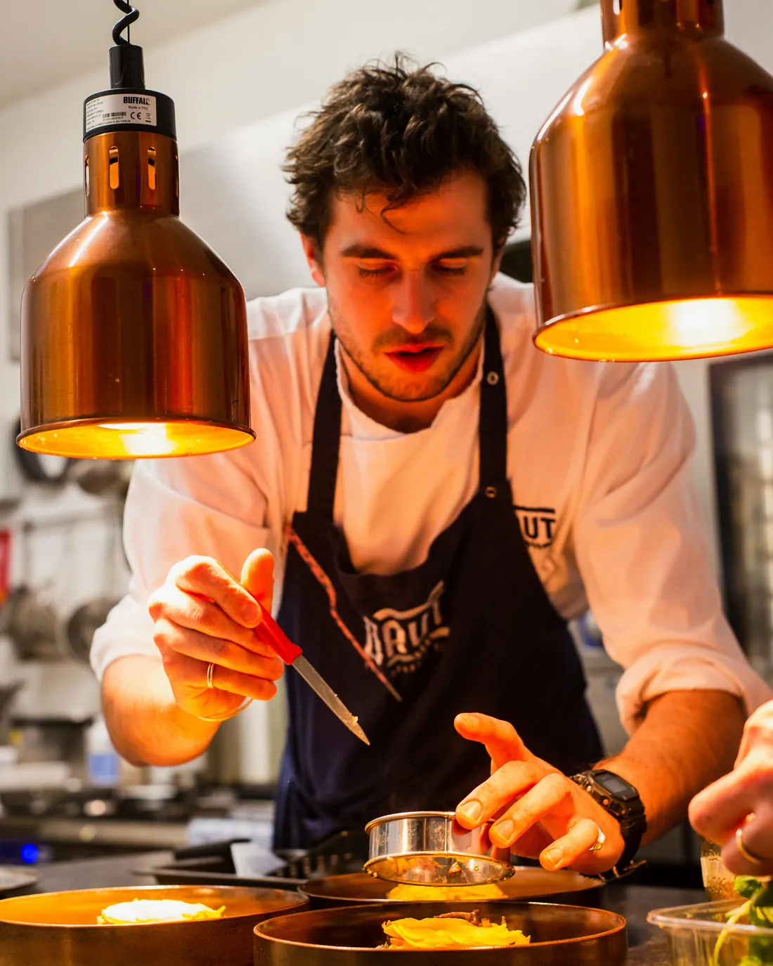 A chef plating dishes under copper lamps
