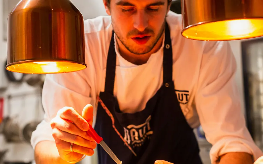 A chef plating dishes under copper lamps
