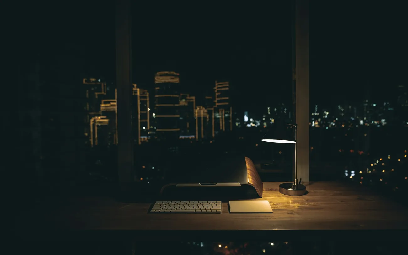 A desk lamp lit at night with the city beyond the window