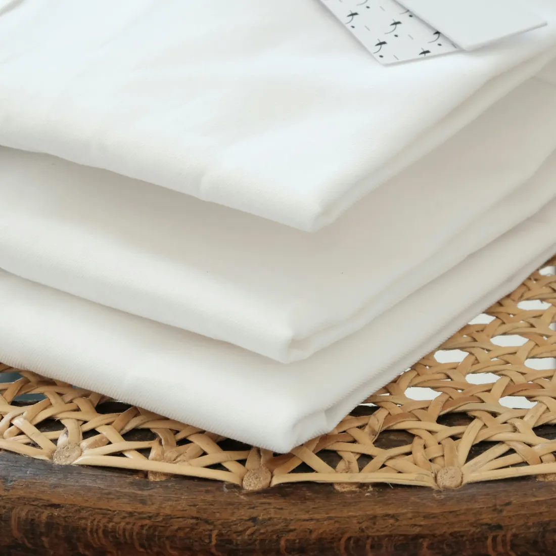 Folded white table linen on a woven tray